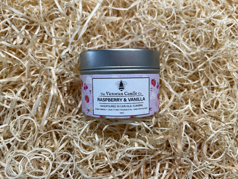 Candle jar labeled 'Raspberry & Vanilla' by The Victorian Candle Co. on a bed of straw.
