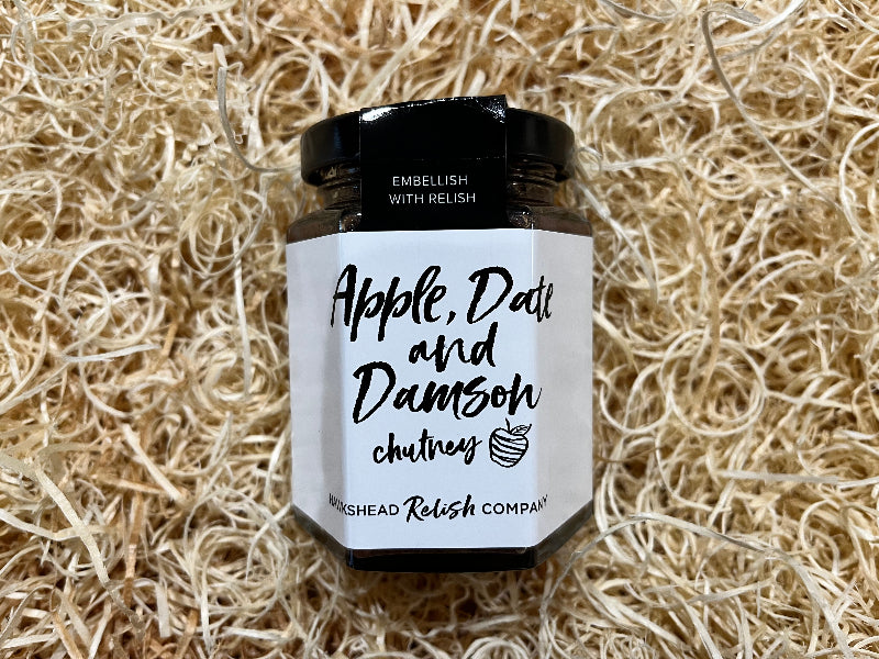 Jar of apple, date, and damson chutney on a textured beige background