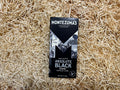 Montezuma's Absolute Black chocolate bar packaging on a straw background