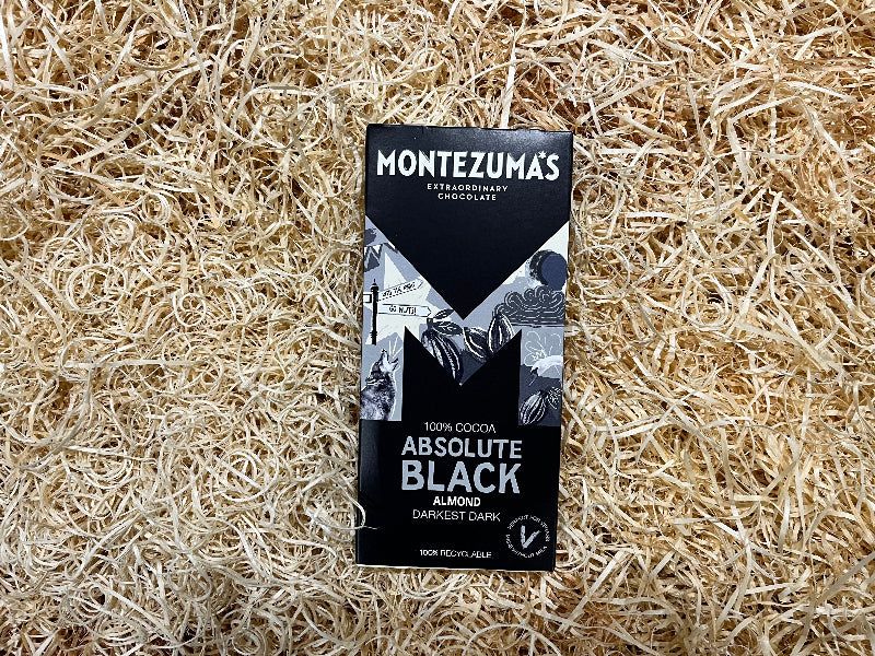 Montezuma's Absolute Black chocolate bar packaging on a straw background