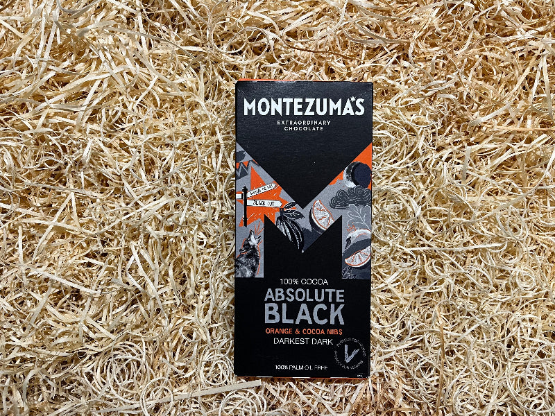 Montezuma's Absolute Black chocolate bar packaging on a textured beige background