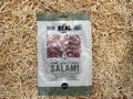Packaged salami with 'The Real' branding on a straw background