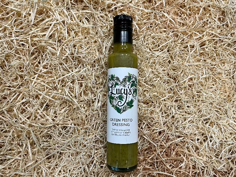 Bottle of Lucy's Green Pesto Dressing on a straw background