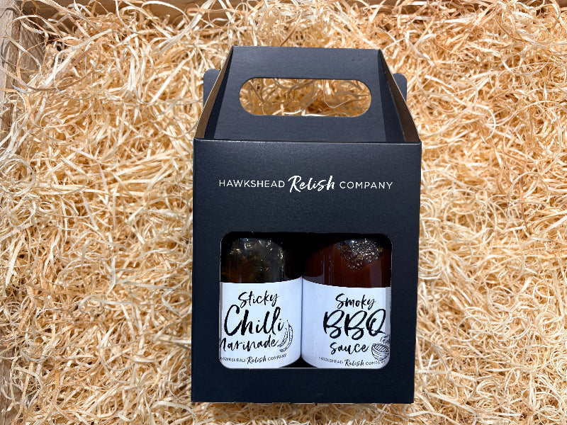 Two bottles of relish in a black carrying box on straw