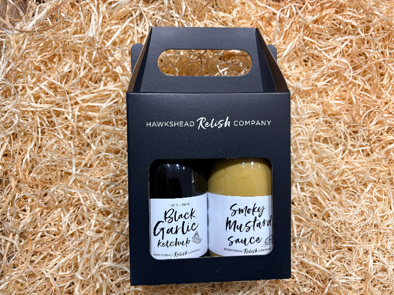 Two bottles of Hawkeshead Relish Company products in a black box on straw background
